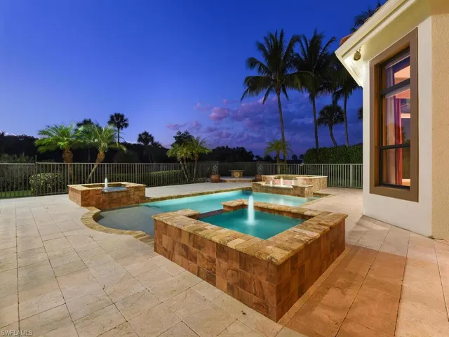 Pool at dusk featuring a patio, a pool with connected hot tub, and a fenced backyard