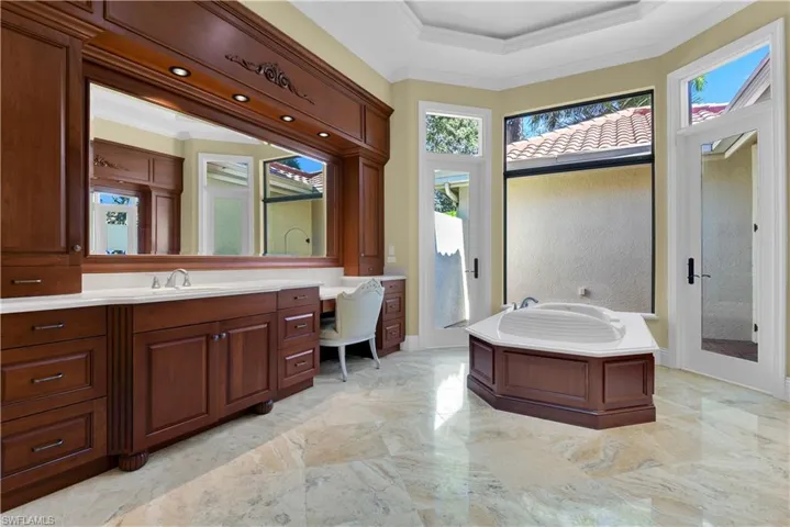 Bathroom with crown molding, vanity, a garden tub, light marble finish floors, and a raised ceiling