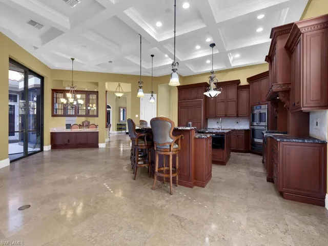 Kitchen featuring a breakfast bar, tasteful backsplash, coffered ceiling, decorative light fixtures, and a chandelier