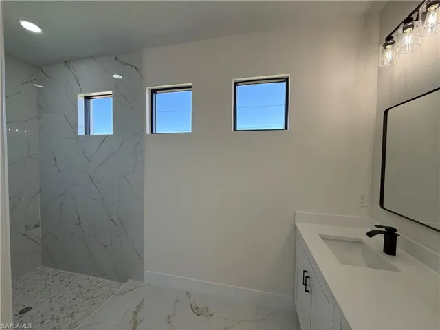Bathroom featuring vanity, a marble finish shower, and light marble finish flooring