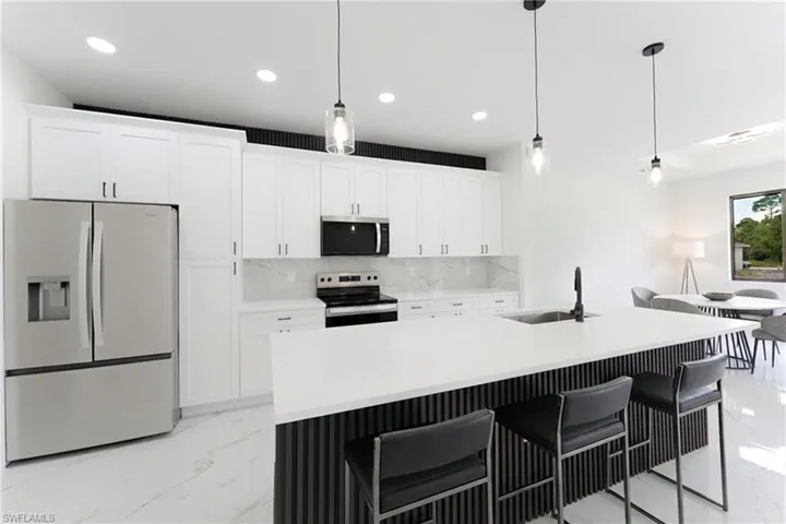 Kitchen with stainless steel appliances, a breakfast bar, white cabinetry, an island with sink, and decorative light fixtures