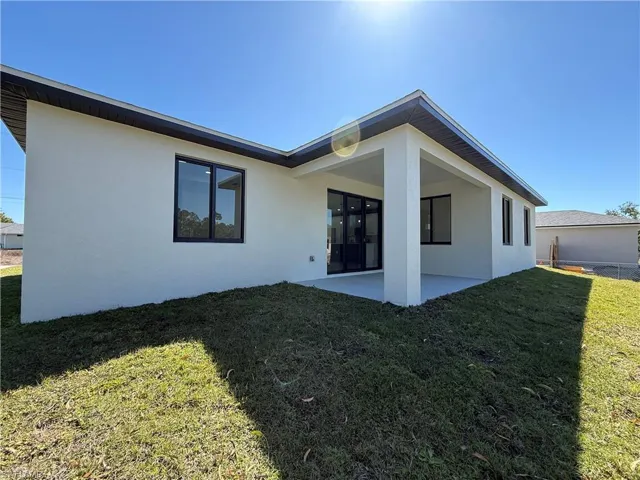 Rear view of house featuring stucco siding, a lawn, and a patio