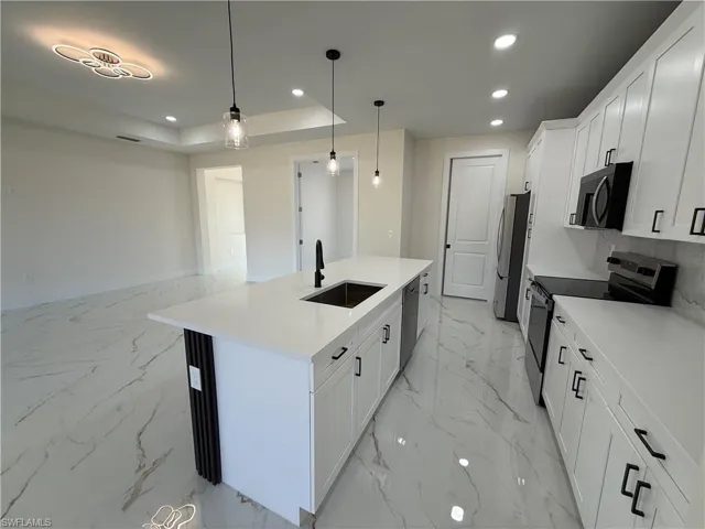 Kitchen featuring white cabinets, stainless steel appliances, decorative light fixtures, a center island with sink, and light stone countertops