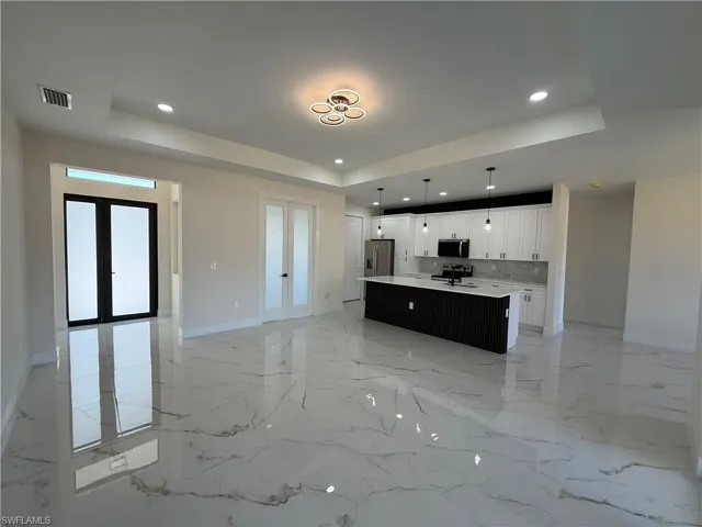 Unfurnished living room with french doors, a raised ceiling, recessed lighting, and light marble finish flooring