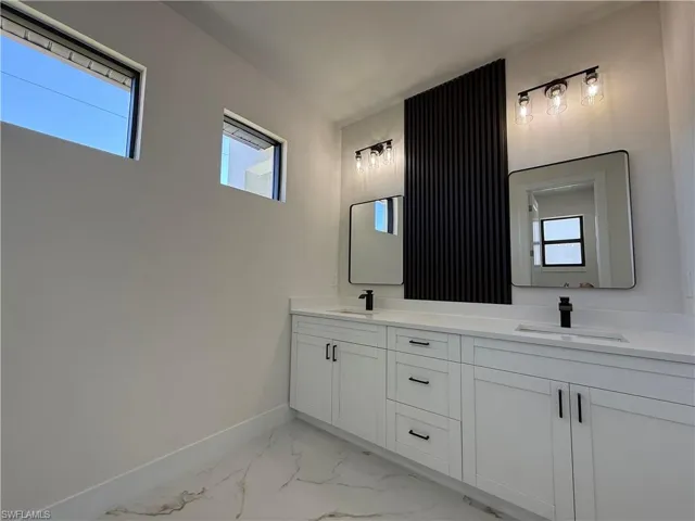 Full bathroom with double vanity, light marble finish floors, and healthy amount of natural light