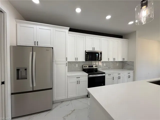 Kitchen with stainless steel appliances, white cabinetry, light marble finish floors, and decorative backsplash