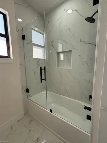 Full bathroom featuring combined bath / shower with glass door and light marble finish flooring