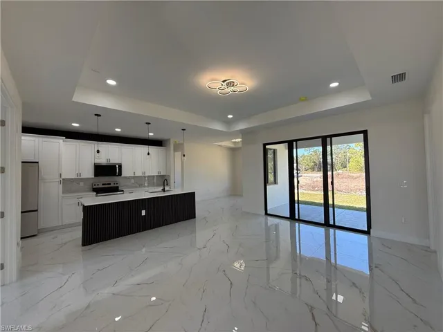 Kitchen with open floor plan, a center island with sink, white cabinetry, hanging light fixtures, and stainless steel appliances