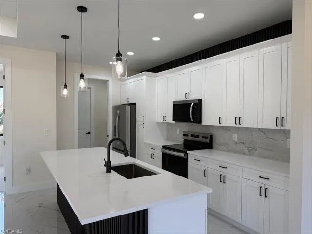 Kitchen with stainless steel appliances, a kitchen island with sink, white cabinets, tasteful backsplash, and pendant lighting