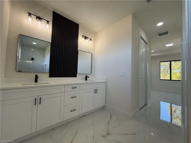 Full bath with double vanity, recessed lighting, and light marble finish flooring