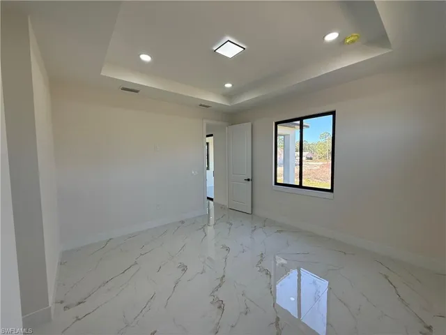 Spare room with recessed lighting, light marble finish floors, and a raised ceiling