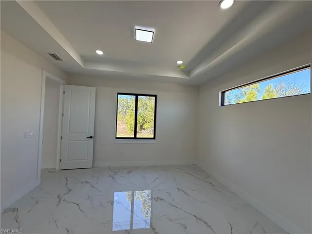 Empty room featuring recessed lighting, a raised ceiling, and light marble finish floors