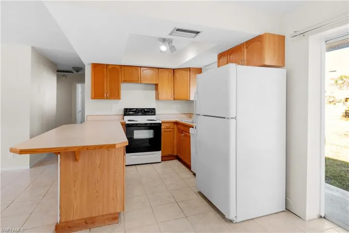 Kitchen featuring a breakfast bar, electric range oven, white refrigerator, kitchen peninsula, and a raised ceiling