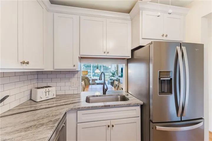 Kitchen with stainless steel appliances, white cabinetry, backsplash, and light stone countertops