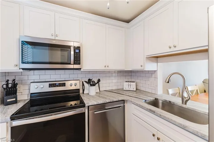 Kitchen featuring stainless steel appliances, white cabinetry, light stone countertops, and decorative backsplash