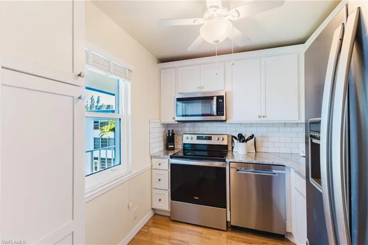 Kitchen featuring white cabinets, stainless steel appliances, ceiling fan, and light stone counters
