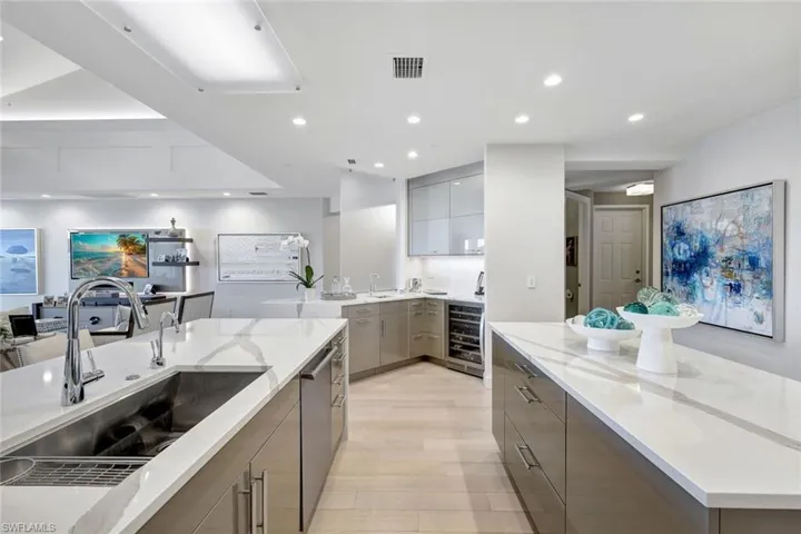 Kitchen with light stone countertops, light wood-type flooring, gray cabinetry, beverage cooler, and sink