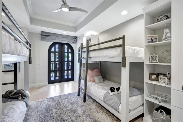 Bedroom featuring ceiling fan, french doors, crown molding, wood-type flooring, and a tray ceiling