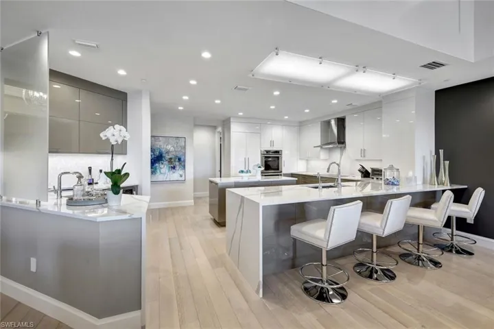 Kitchen featuring gray cabinetry, a kitchen breakfast bar, oven, wall chimney range hood, and light hardwood / wood-style floors