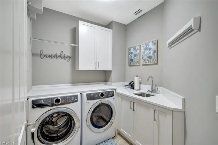Laundry room featuring washer and clothes dryer, sink, light tile patterned floors, and cabinets