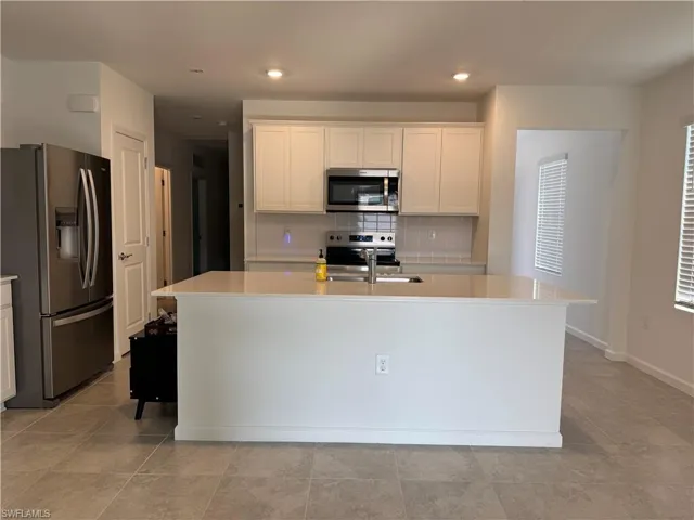 Kitchen featuring stainless steel appliances, white cabinetry, an island with sink, tasteful backsplash, and light stone countertops
