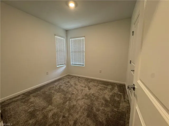 Empty room featuring baseboards and dark colored carpet