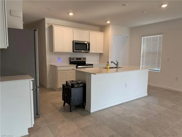 Kitchen with stainless steel appliances, white cabinetry, recessed lighting, a kitchen island with sink, and light stone counters