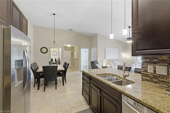 Kitchen featuring dark wood finish cabinetry, stainless steel appliances, light stone counters, decorative backsplash, and decorative light fixtures