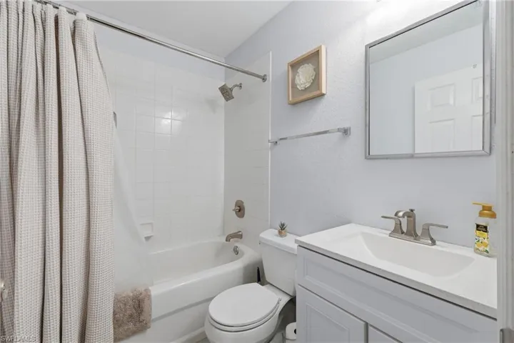 Full bath with a textured wall, shower / bath combo with shower curtain, and vanity