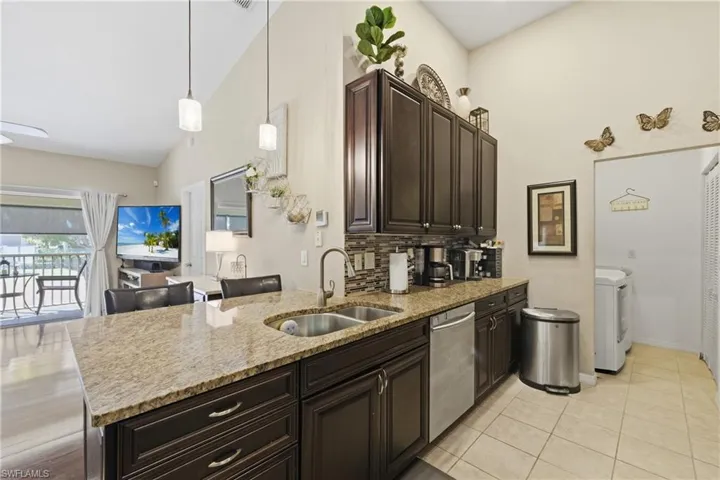 Kitchen featuring dark wood finish cabinetry, light stone counters, vaulted ceiling, hanging light fixtures, and tasteful backsplash