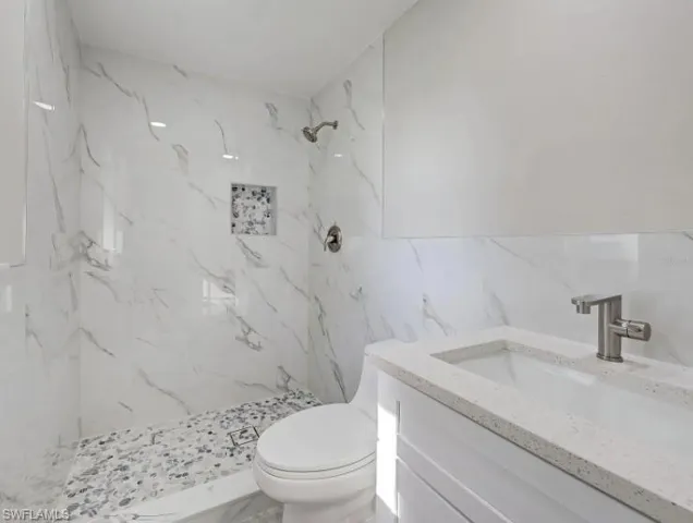 Full bath featuring a marble finish shower, vanity, and tile walls