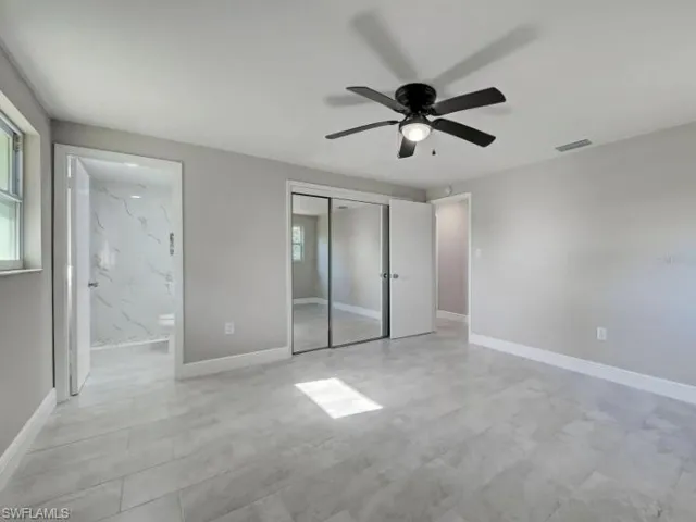 Unfurnished bedroom with multiple windows, a closet, ceiling fan, and ensuite bath