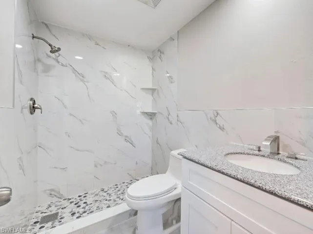 Bathroom with a marble finish shower, vanity, and tile walls