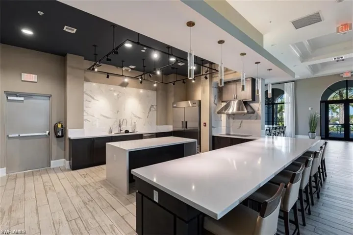 Kitchen featuring hanging light fixtures, light stone counters, dark cabinets, a breakfast bar, and stainless steel built in fridge
