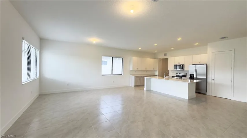 Kitchen featuring open floor plan, appliances with stainless steel finishes, an island with sink, recessed lighting, and white cabinets