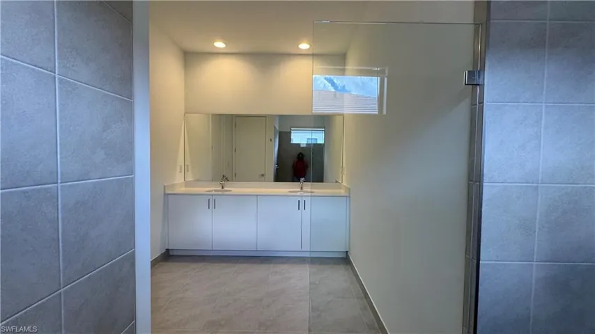 Bathroom with double vanity, recessed lighting, light tile patterned floors, tile walls, and a shower