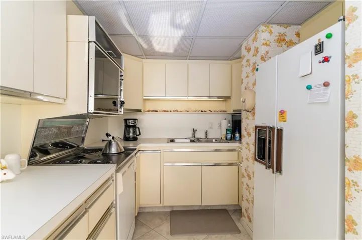 Kitchen with cream cabinetry, white appliances, light countertops, and light tile patterned floors