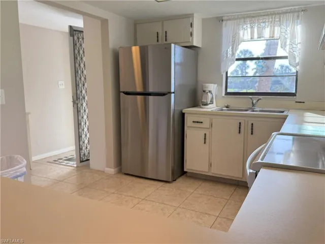 Kitchen with light tile patterned floors, stove, stainless steel refrigerator, and sink