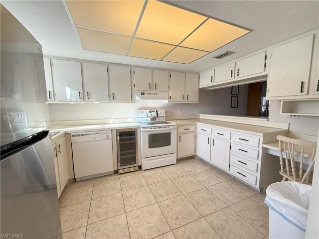 Kitchen with light tile patterned floors, white appliances, and beverage cooler