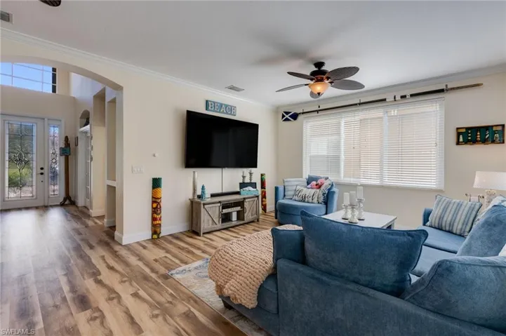 Living area with ornamental molding, arched walkways, ceiling fan, and wood finished floors