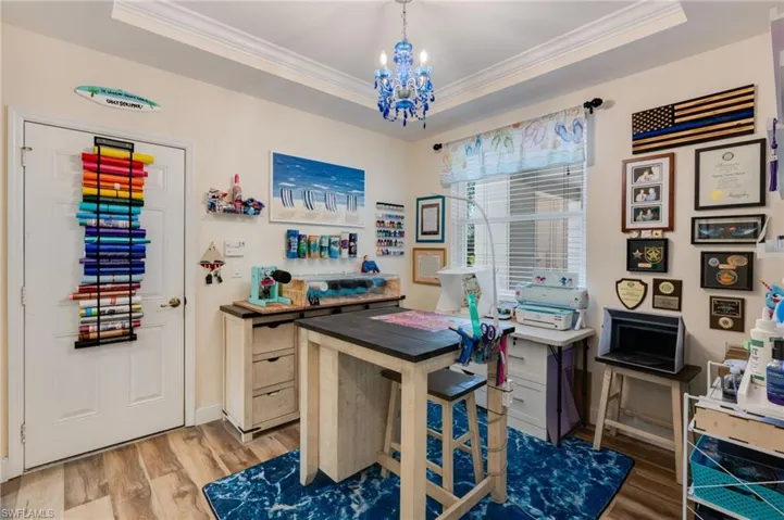 Office space featuring a chandelier, crown molding, light wood-type flooring, and a raised ceiling