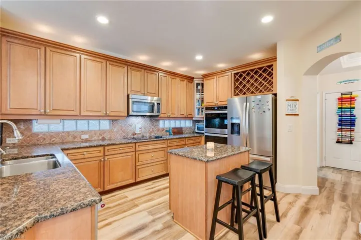 Kitchen with arched walkways, light wood finished floors, a kitchen island, appliances with stainless steel finishes, and recessed lighting