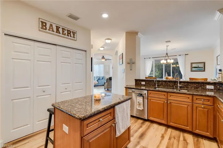 Kitchen featuring brown cabinetry, dark stone countertops, a kitchen bar, stainless steel dishwasher, and recessed lighting