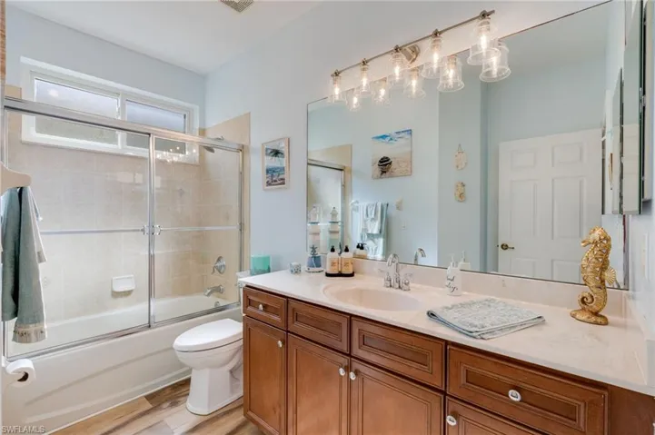 Bathroom featuring vanity, bath / shower combo with glass door, and light wood-type flooring