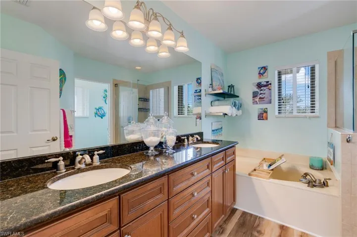 Full bath with double vanity, a garden tub, an enclosed shower, and light wood finished floors