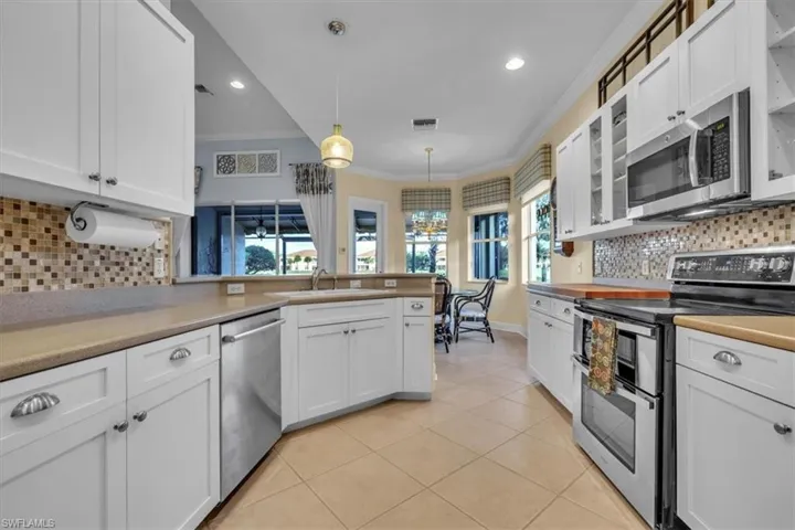 Kitchen featuring white cabinetry, solid surface countertops, mosaic tile backsplash, stainless steel appliances, and ceramic tile flooring