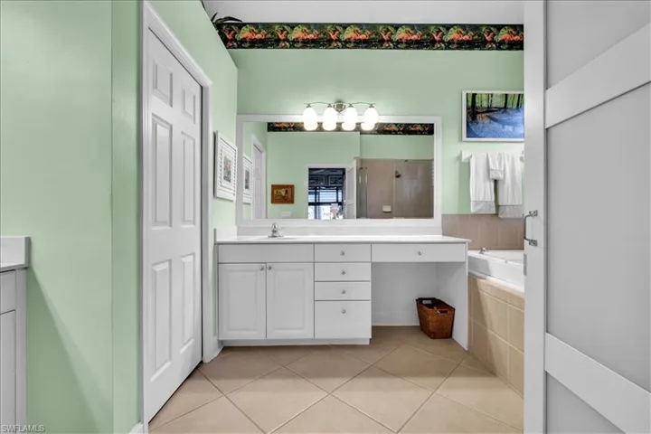 Bathroom featuring a white vanity with integrated cabinetry and drawers, a large framed wall mirror, five-light fixture, and tile flooring