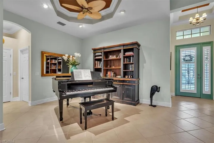 Tray ceiling with recessed lighting and ceiling fan, built-in wooden cabinetry, tile flooring, and arched entryway