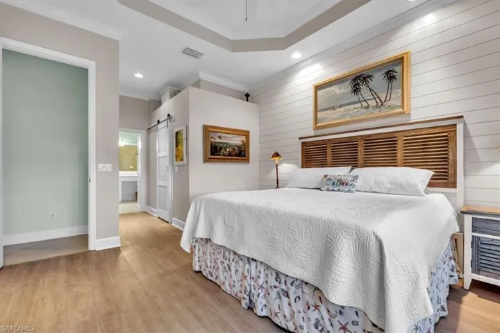 Tray ceiling, wood-finish flooring, horizontal shiplap accent wall, and sliding barn-style door