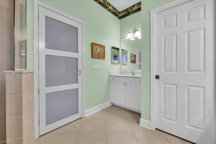 Bathroom featuring white vanity with integrated basin, frosted glass panel door, tile flooring, and wall-mounted vanity lighting